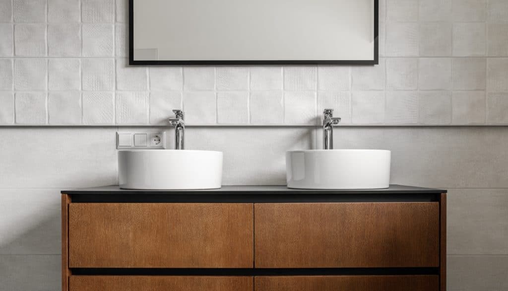 Bathroom modern vanity unit with two round ceramic sinks, chrome faucets and mirror with black frame, white tales and wooden cabinet. Contemporary bathroom interior in minimalist Scandinavian style